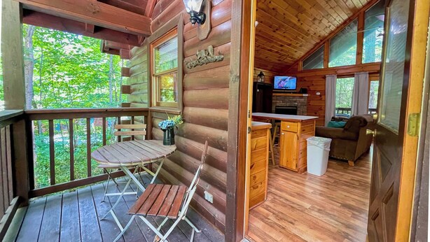 A wooden cabin with a porch, a dining area, a kitchen, and a television.