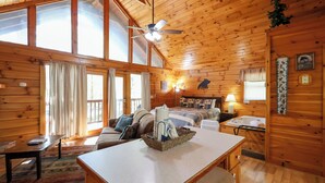 A wooden cabin with a dining area, a bed, a bathroom, and a large window.