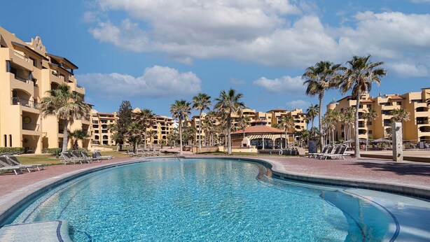 Una piscina rodeada de palmeras y un edificio de resort con varios balcones.