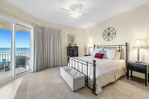 Una camera da letto con un letto, una panca, un comodino, una lampada, una ventola a soffitto e vista sull'oceano attraverso una porta scorrevole in vetro.