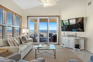 En rummelig stue med et stort skydedørsparti, der fører til en udendørs balkon, et stort fladskærms-tv på væggen og et hyggeligt siddeområde med sofa og sofabord.