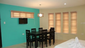 A room with a bed, a dining table with chairs, a TV mounted on the wall, and windows with blinds. - El Vistra Travellers Inn & Coffee Shop (Calumpit)