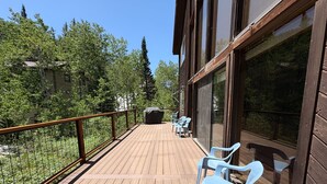 A wooden deck with chairs and a covered grill area, overlooking a forested area. - Storm Mountain Escape by Cottonwood Lodging (Brighton)