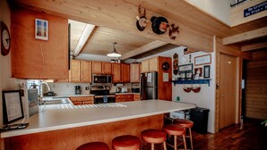 A kitchen with wooden cabinets, a large island with stools, and a ceiling with wooden beams. - Storm Mountain Escape by Cottonwood Lodging (Brighton)