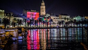 Un paisaje urbano frente al agua, con una torre destacada y edificios iluminados.