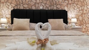 Una cama bien tendida con un arreglo de toallas en forma de corazón, un edredón estampado y una pared con textura de piedra.