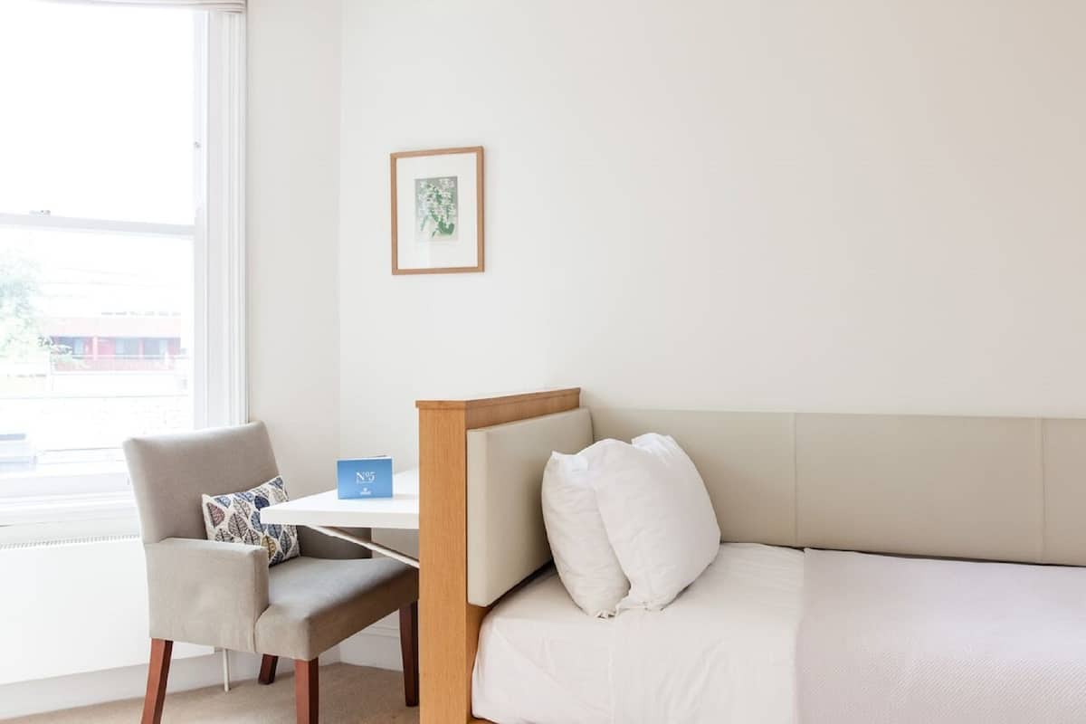 Una habitación con cama, una silla, una mesita y una ventana.