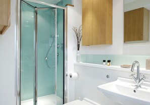 Un baño moderno con cabina de ducha de vidrio, un lavamanos blanco con un solo grifo y armarios de madera sobre el espejo.
