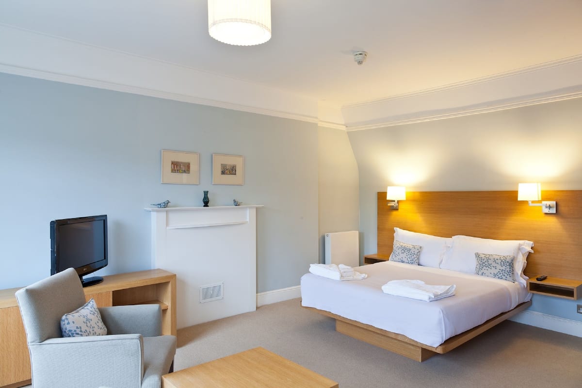 Habitación de hotel con cama, escritorio, silla, televisión y dos lámparas de pared.