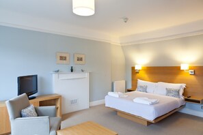 Habitación de hotel con cama, escritorio, silla, televisión y dos lámparas de pared.