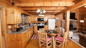 Interior de una cabaña de madera con cocina, comedor y chimenea.
