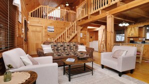 Interior acogedor de una cabaña de madera, con sala de estar que incluye dos sofás, una mesa de centro y una escalera que sube a un nivel superior.