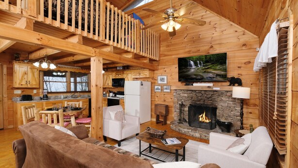 Interior acogedor de una cabaña con chimenea, muebles de madera y un televisor montado en la pared.