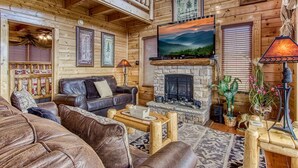 A cozy log cabin interior with a fireplace, leather sofas, and framed artwork.