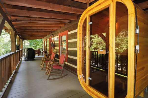 A wooden cabin with a porch, rocking chairs, and a covered grill area.