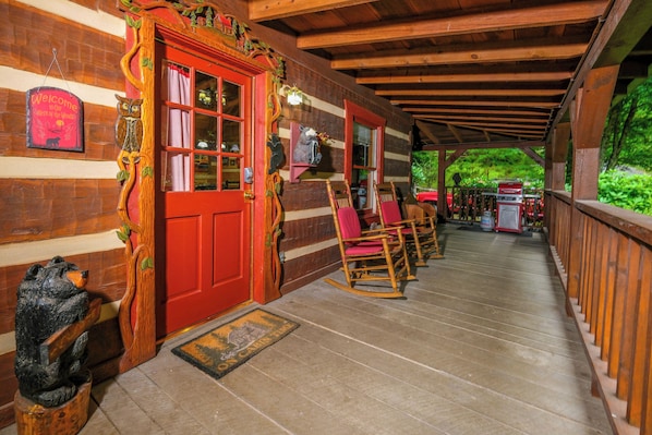 A wooden cabin with a red door, rocking chairs, and a porch.
