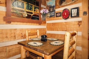 A wooden interior with a table, chairs, a clock, and a bear figurine.