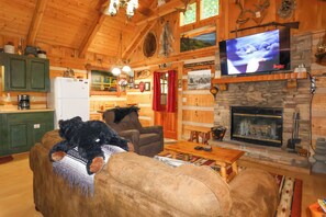 A cozy cabin interior with a fireplace, wooden walls, a television, and a plush sofa.