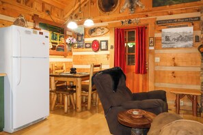 A rustic cabin interior with a wooden dining table, a refrigerator, and a cozy seating area.