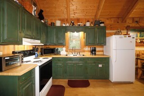 A kitchen with green cabinets, a white refrigerator, a stove, a microwave, and a coffee maker.