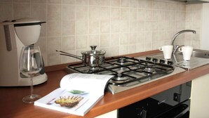A kitchen with a gas stove, a coffee maker, and a wine glass.