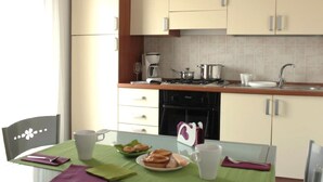 A modern kitchen with a gas stove, coffee maker, and a sink. There is a dining table with a green tablecloth and a chair.