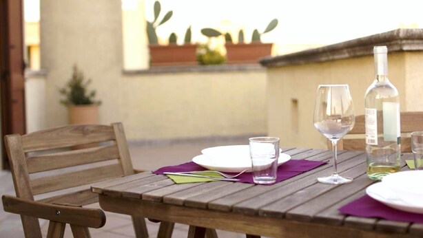 A wooden table set with plates, glasses, and a bottle, with a potted plant in the background.