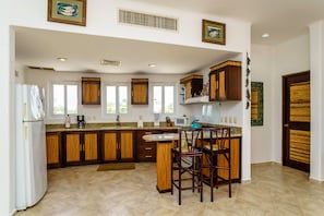 A kitchen with wooden cabinets, a refrigerator, and a bar area with stools. - Las Tortugas A3 - beautiful 2 bedrooms condo on a beach side access in down town (Benito Juarez)