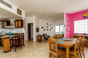 A spacious kitchen with wooden cabinets, a dining area with a wooden table and chairs, and a bright pink accent wall. - Las Tortugas A3 - beautiful 2 bedrooms condo on a beach side access in down town (Benito Juarez)