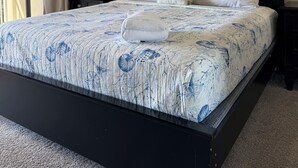 Een slaapkamer met een bed, nachtkastje, lamp, plafondventilator en raam met gordijnen.