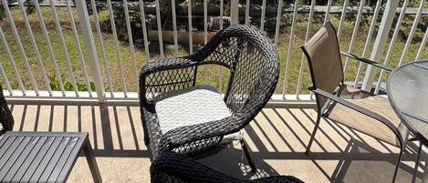 A balcony with wicker chairs and a table, overlooking a body of water and greenery.