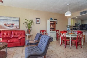 A living room with a red sofa, a blue armchair, and a dining area with red chairs and a white table.