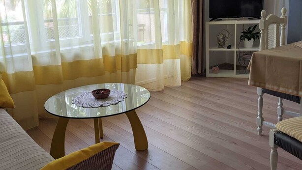 A living room with a glass coffee table, a sofa, a TV on a stand, and a bookshelf.