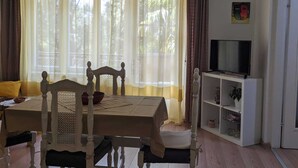 A room with a dining table, chairs, a television on a stand, and a bookshelf.