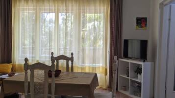 A room with a dining table, chairs, a television on a stand, and a bookshelf.