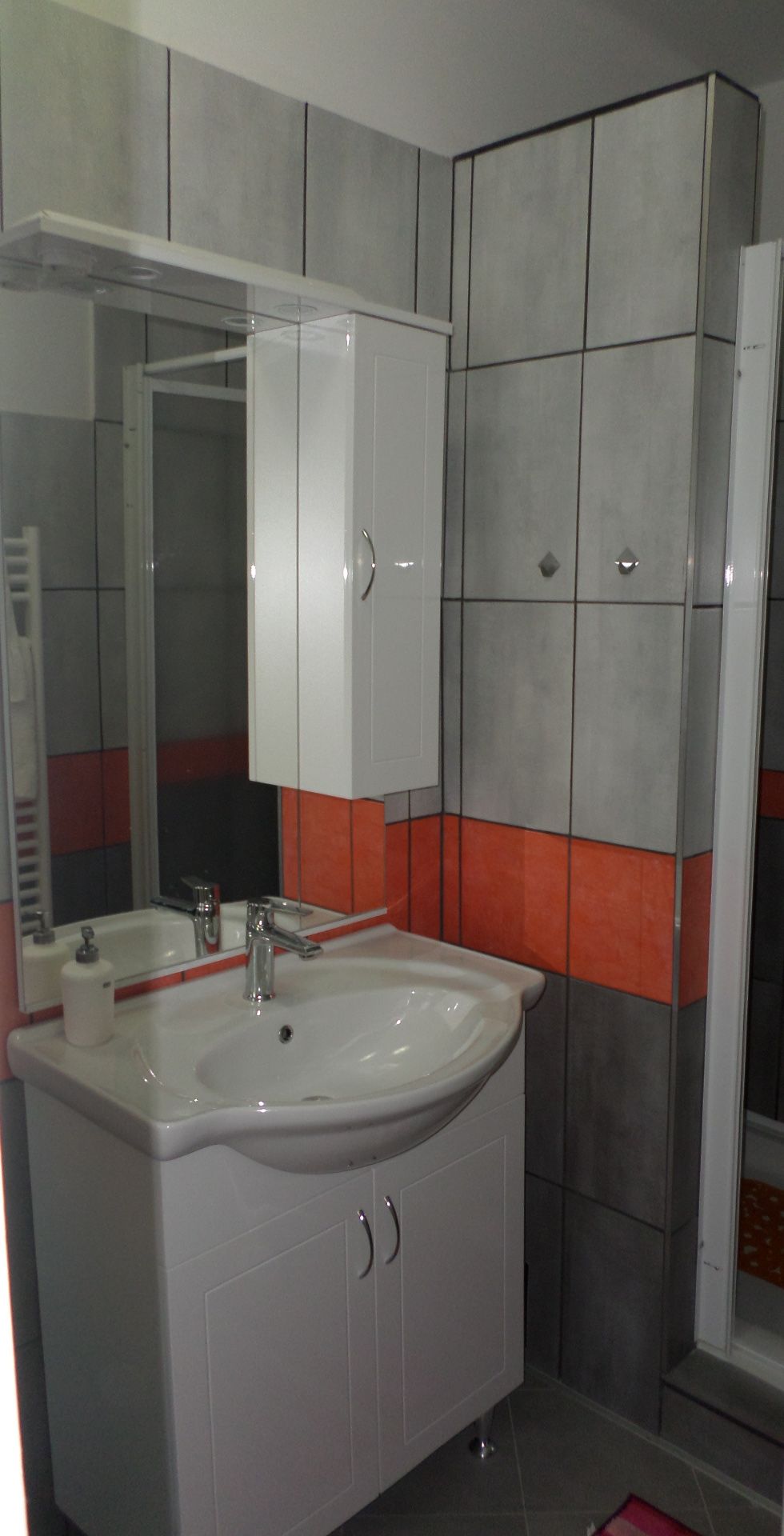 A bathroom with a white sink, mirror, and cabinet, tiled walls, and a shower area.