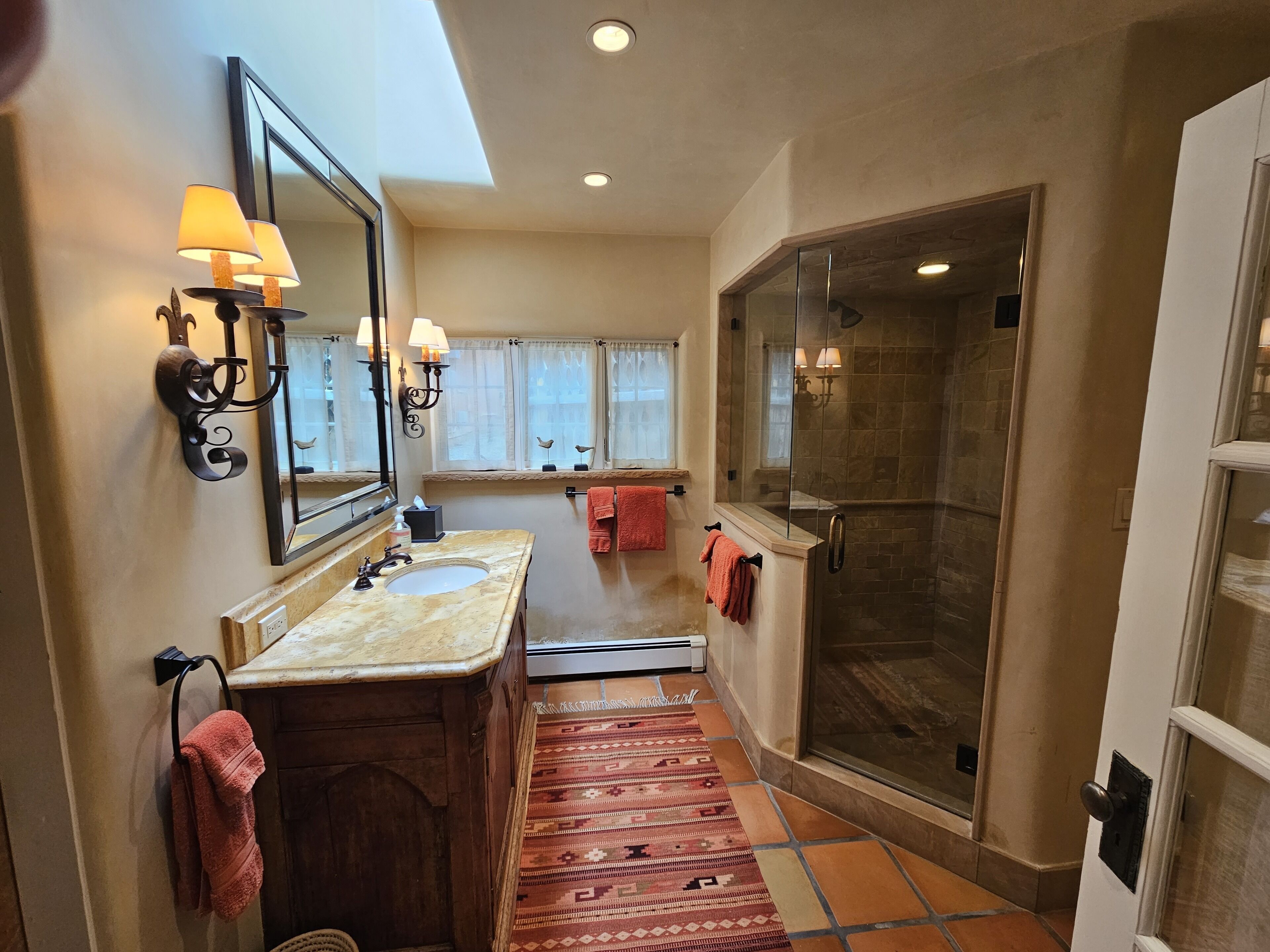 A bathroom with a double sink, a large mirror, a glass shower enclosure, and a patterned rug.