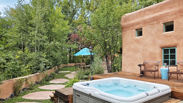 A hot tub in a garden with stone paths, wooden deck, and outdoor furniture.