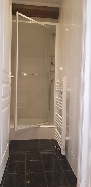 Un espace douche doté d’une porte en verre, d’un porte-serviettes blanc et d’un sol carrelé noir.