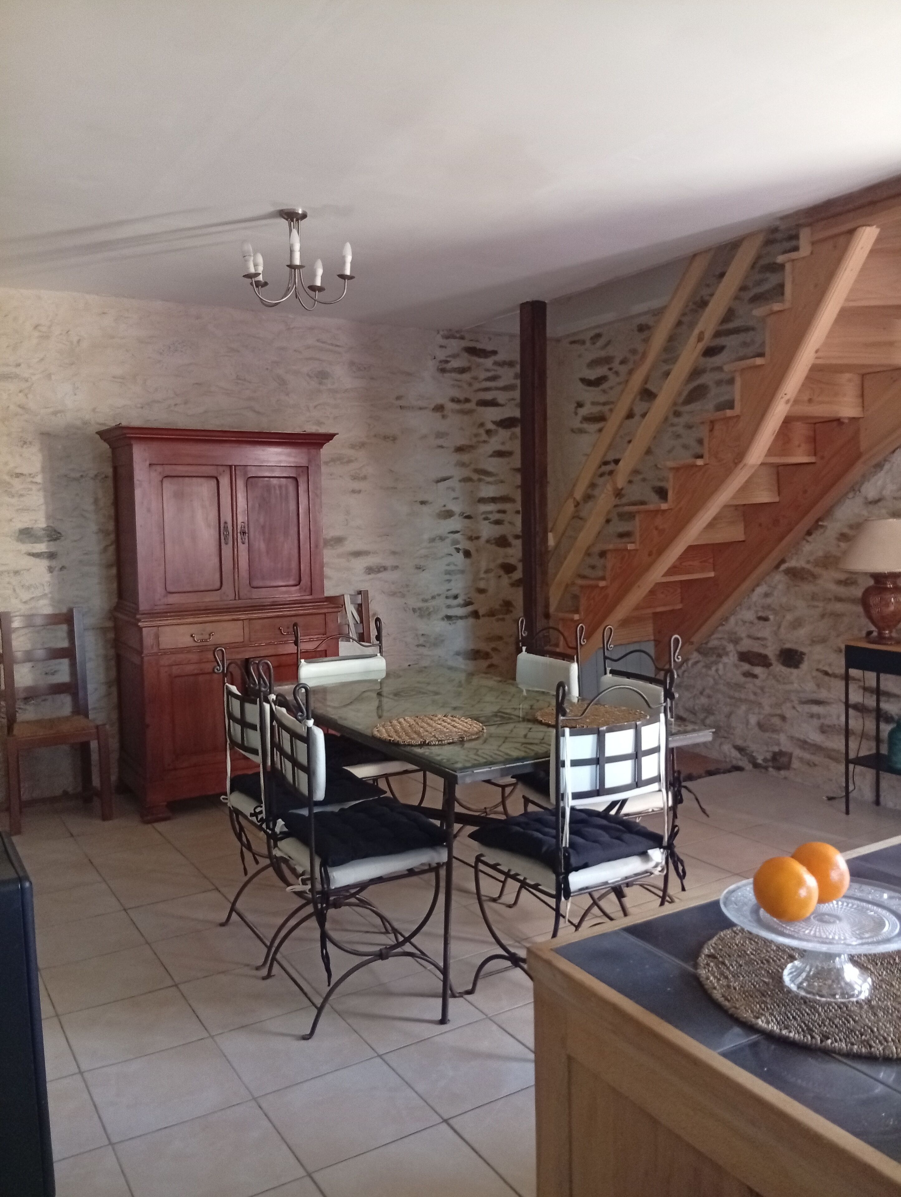 Un comedor con una mesa de vidrio, sillas de metal, un armario de madera y una escalera con peldaños de madera.