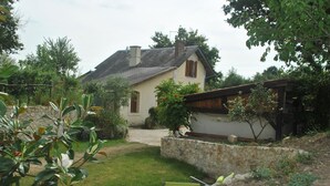 Ein Haus mit einer Steinwand, einem Garten mit Rasen und einer Holzpergola.
