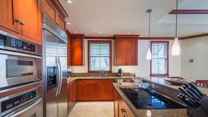 A modern kitchen with stainless steel appliances, wooden cabinets, granite countertops, and pendant lighting. - 2 BR rental with a nice tropical view - Hilton Waikoloa Access Included (Waikoloa)