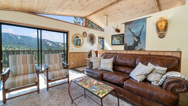 A spacious living area with a leather couch, striped armchairs, a coffee table, and a large window offering a scenic mountain view. - BEAUTIFUL VIEWS, Cute 1,200 sq ft, HOT TUB! Close to slopes & Lake! FENCED YD (Big Bear Lake)