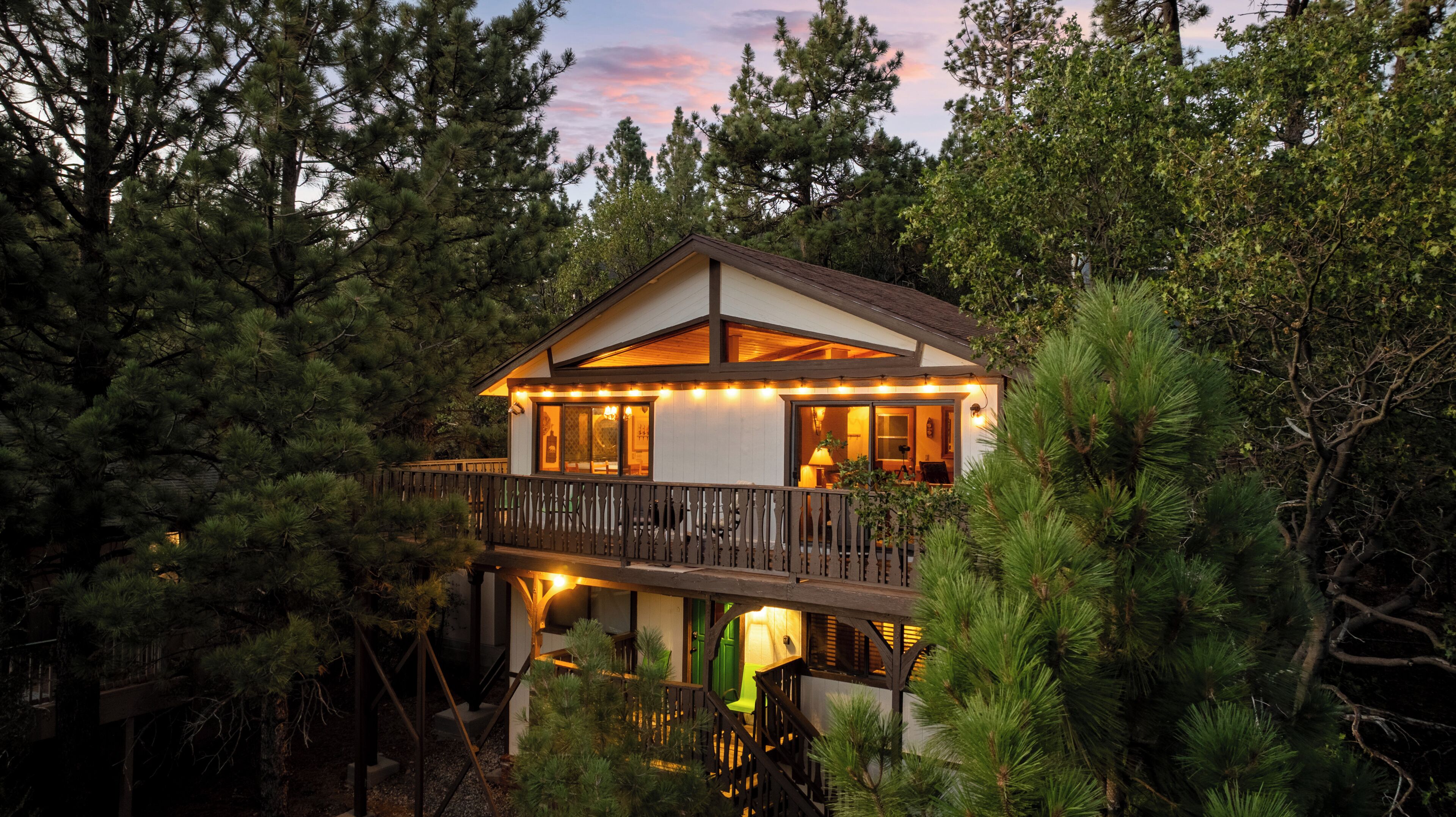 Une cabane en bois à deux étages, dotée d’un balcon et entourée d’une forêt dense.