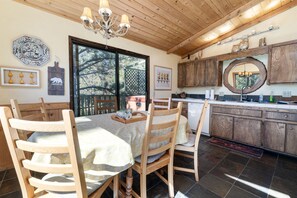 A dining area with a wooden table and chairs, a chandelier, and a kitchen with wooden cabinets and a large mirror.