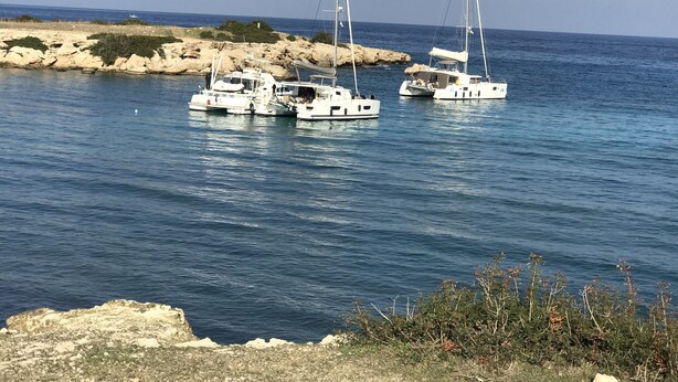 Drie zeilboten aangemeerd langs een rotsachtige kust met helderblauw water.