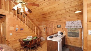 L’intérieur d’un chalet en bois comprend un coin repas, une cuisine et un escalier.