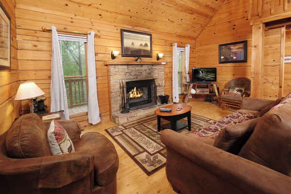 A cozy cabin interior with a fireplace, wooden walls, a television, and comfortable seating. - 2 king bedrooms, hot tub, great location! (Sevierville)