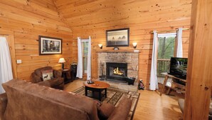 Un intérieur de chalet chaleureux avec une cheminée, des murs en bois, un canapé et un téléviseur.