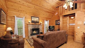 L’intérieur d’un chalet confortable, avec une cheminée, des murs en bois, un canapé et un téléviseur.